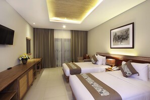 A hotel room with two beds, a desk, a television, a framed picture on the wall, and a window with curtains. - Radha Phala Resort and Spa (Ubud)