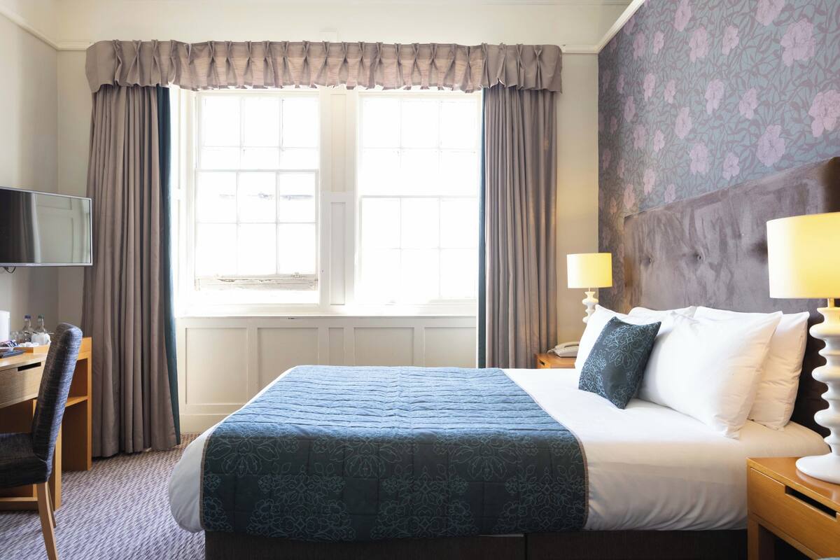 A hotel room with a large bed, a desk, a television, and a window with curtains.