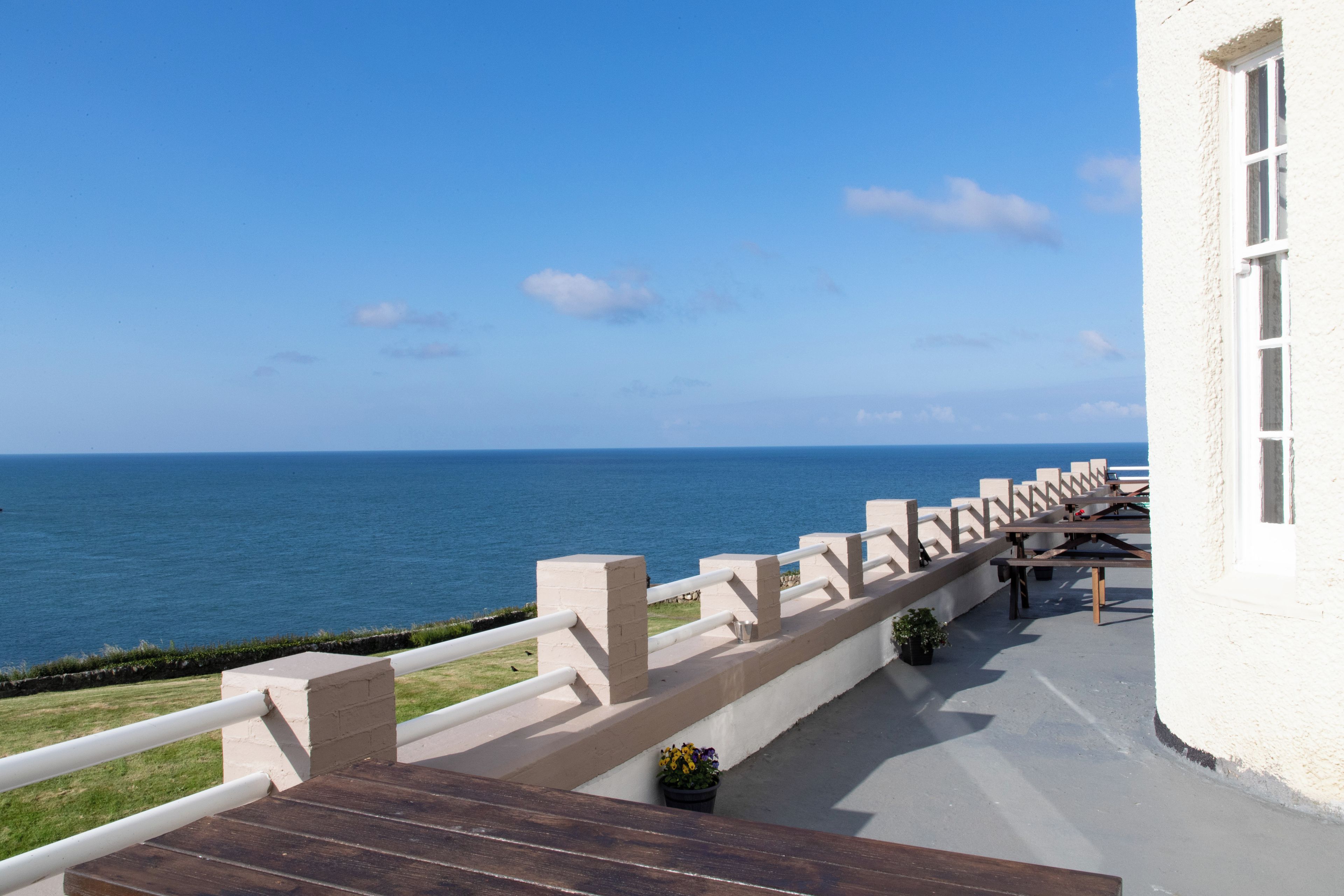 A balcony with a view of the sea, a white building, and a wooden deck.