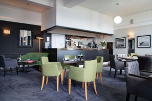 Eine moderne Hotelhalle mit Barbereich, Sitzgelegenheiten und einer Wanduhr.