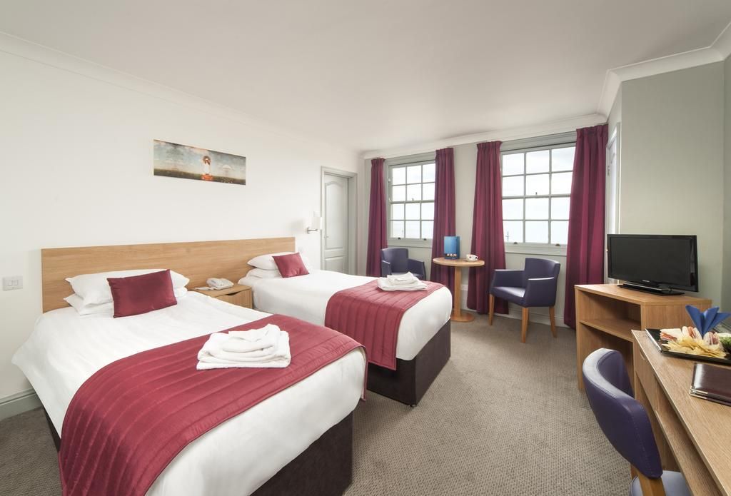 Ein Hotelzimmer mit zwei Betten, einem Schreibtisch, einem Stuhl, einem Fernseher und einem Fenster mit Vorhängen.