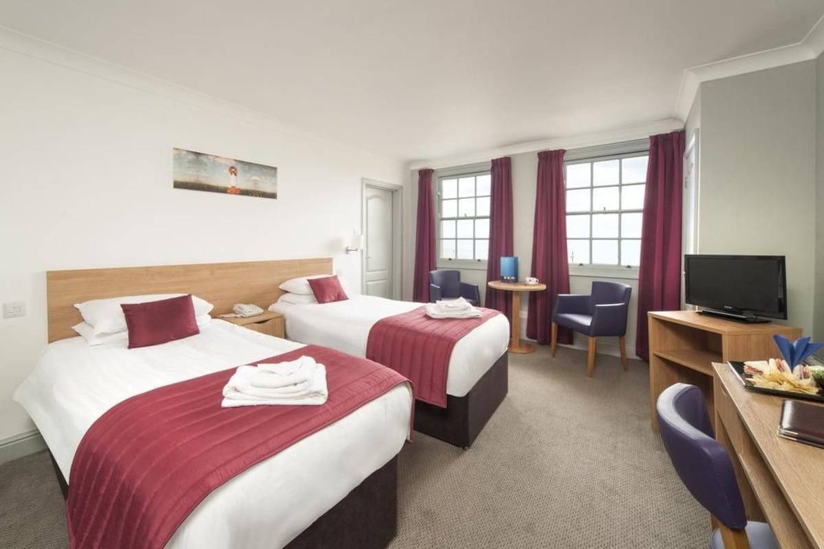 Ein Hotelzimmer mit zwei Betten, einem Schreibtisch, einem Stuhl, einem Fernseher und einem Fenster mit Vorhängen.