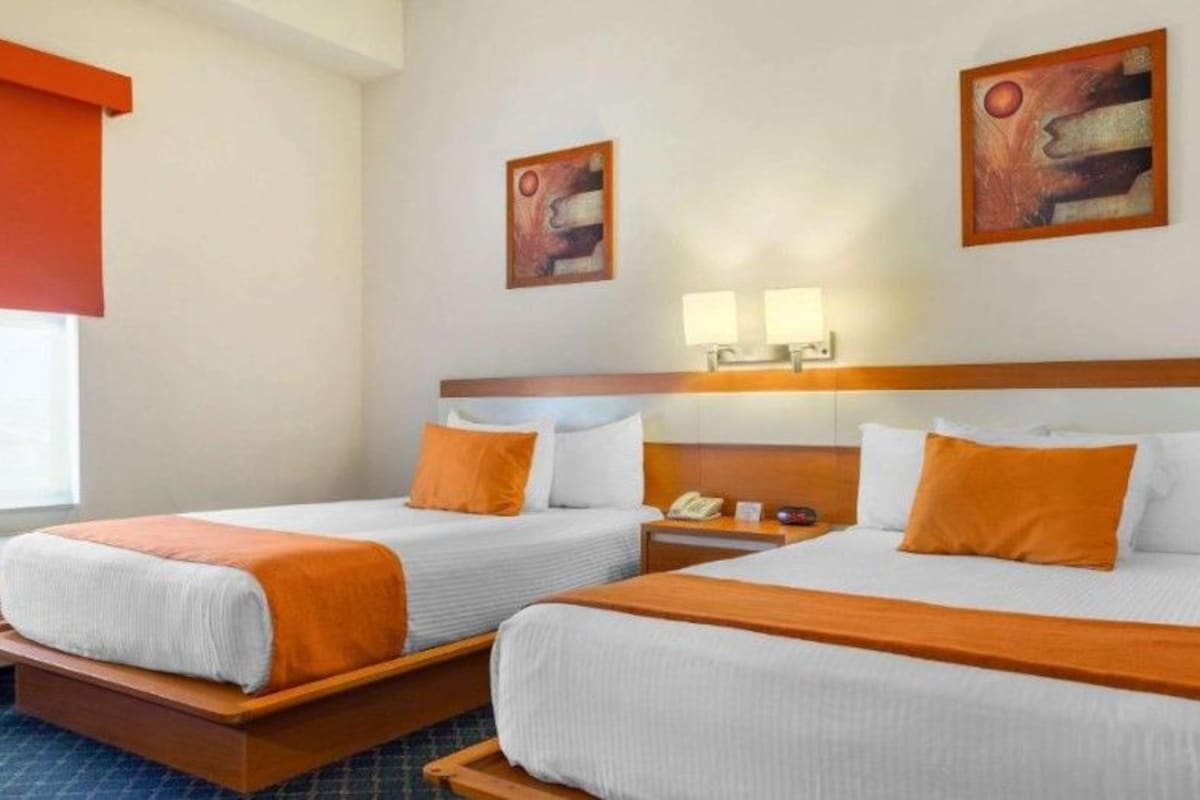 Habitación de hotel con dos camas, una mesita de noche, una lámpara y obras de arte en la pared.