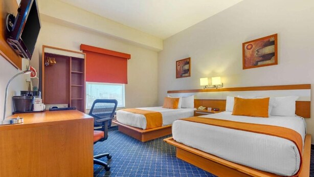A hotel room with two beds, a desk, a chair, a TV, a closet, and artwork on the walls. - Greenwood Hotel Torreon (Torreón)