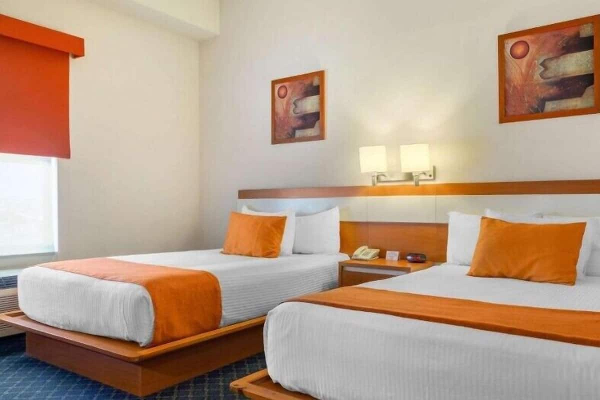 Habitación de hotel con dos camas, una mesita de noche, una lámpara y obras de arte en la pared.