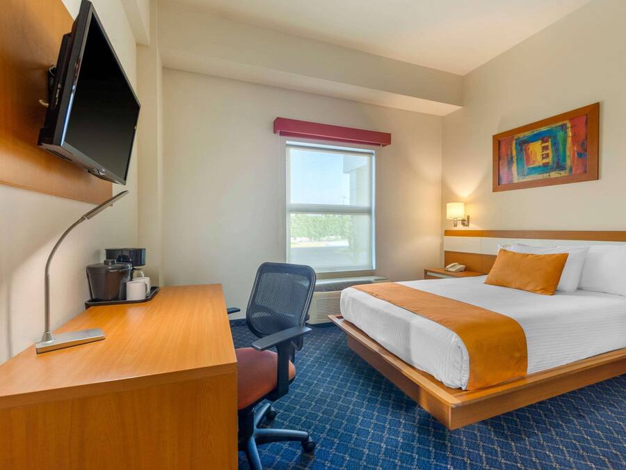 Habitación de hotel con cama, escritorio, silla, televisión, ventana y una obra de arte en la pared.