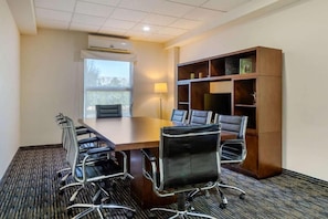 A conference room with a large table, six chairs, a bookshelf, an air conditioning unit, and a window. - Greenwood Hotel Torreon (Torreón)
