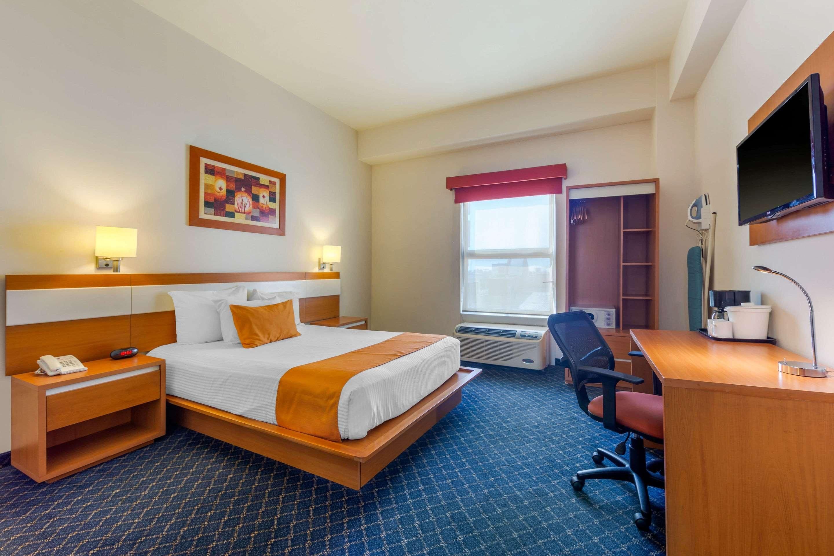 Ein Hotelzimmer mit einem Bett, Nachttischen, einem Schreibtisch, einem Sessel, einem Fernseher und einem fenster mit Vorhängen.