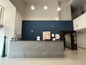 A reception desk with a blue wall, a door, and a security camera. - Greenwood Hotel Torreon (Torreón)