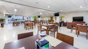 A hotel dining area with multiple tables and chairs, a television, and a sofa. - Greenwood Hotel Torreon (Torreón)