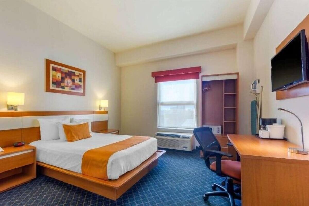 Habitación de hotel con cama, lámparas de noche, escritorio, silla, televisor y ventana con vistas.