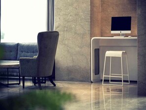 A modern office space with a sofa, a chair, a desk with a computer monitor, and a white stool. - Mercure Chennai Sriperumbudur (Tirukalukundram)