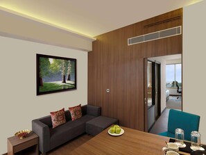 A modern room with a sofa, a dining table with apples and glasses, a painting of a forest, and a view through a door. - Mercure Chennai Sriperumbudur (Tirukalukundram)
