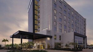 A modern hotel building with a prominent 'Mercure Hotel' sign, a covered entrance, and a landscaped outdoor area with plants. - Mercure Chennai Sriperumbudur (Tirukalukundram)