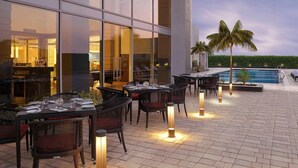 An outdoor dining area with tables and chairs, a pool, and a building with large windows. - Mercure Chennai Sriperumbudur (Tirukalukundram)