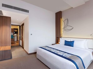 A hotel room with a bed, a wooden wardrobe, a kitchenette, and a wall with a light fixture.