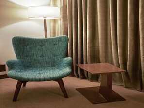 A teal armchair with wooden legs, a small wooden side table, and a floor lamp. - Mercure Chennai Sriperumbudur (Tirukalukundram)
