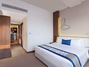 Une chambre d’hôtel avec un lit, une armoire en bois, une kitchenette et un mur muni d’un luminaire.