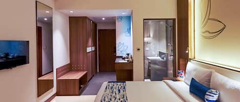A hotel room with a large bed, a TV, a wooden wardrobe, a bathroom with a mirror, and a wall with a decorative design.