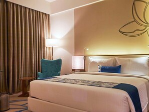 A hotel room with a large bed, a desk, a chair, a lamp, and a curtain. - Mercure Chennai Sriperumbudur (Tirukalukundram)