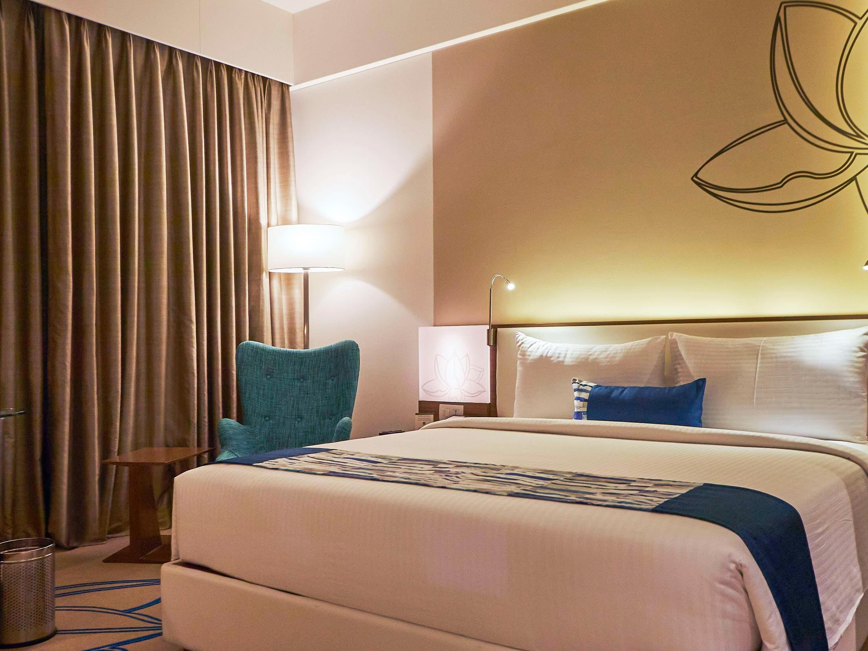 Una habitación de hotel con una cama grande, un escritorio, una silla, una lámpara y una cortina.