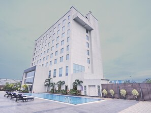 A modern hotel with a pool area, lounge chairs, and a large building with multiple floors and windows. - Mercure Chennai Sriperumbudur (Tirukalukundram)