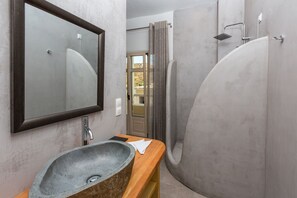 Une salle de bain avec un lavabo en pierre, un grand miroir, une douche avec un pommeau de douche amovible et une vue sur l’extérieur.