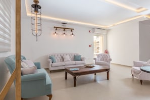 A modern living room with a sofa, armchairs, a coffee table, and pendant lighting. - Anamar Kea (Kea)
