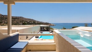 Zona de piscina en la azotea con vista al mar, un área de estar cubierta y una piscina de color azulado.