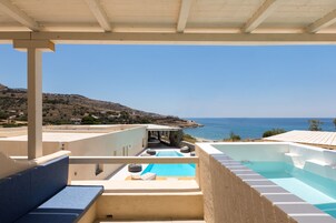 Zona de piscina en la azotea con vista al mar, un área de estar cubierta y una piscina de color azulado.