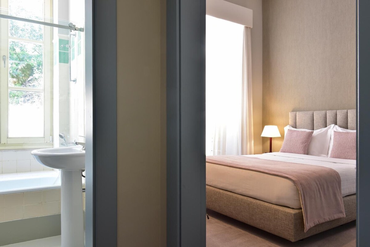 Habitación de hotel con cama, lámpara de noche y vistas al exterior.
