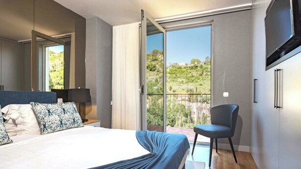 Un dormitorio moderno con una cama grande, una silla, un televisor y un balcón con vistas a las colinas.