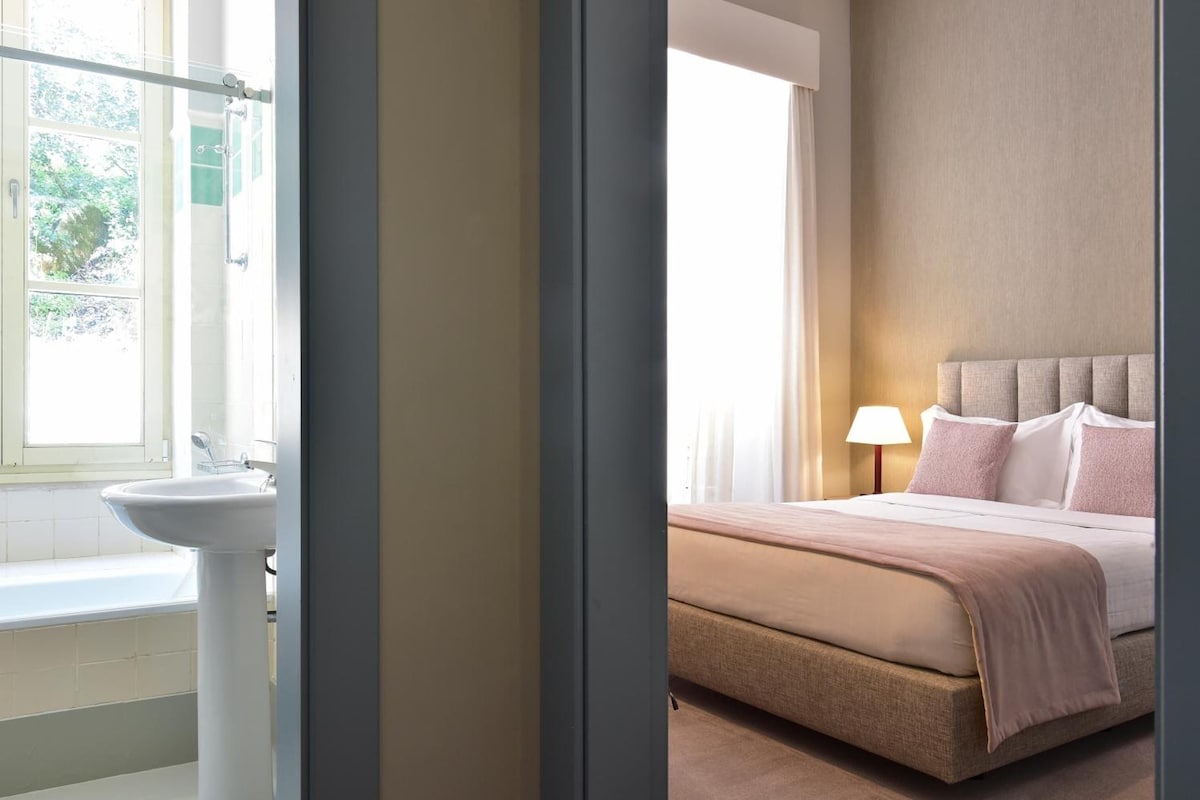 Quarto de hotel com cama, abajur e vista para o exterior.