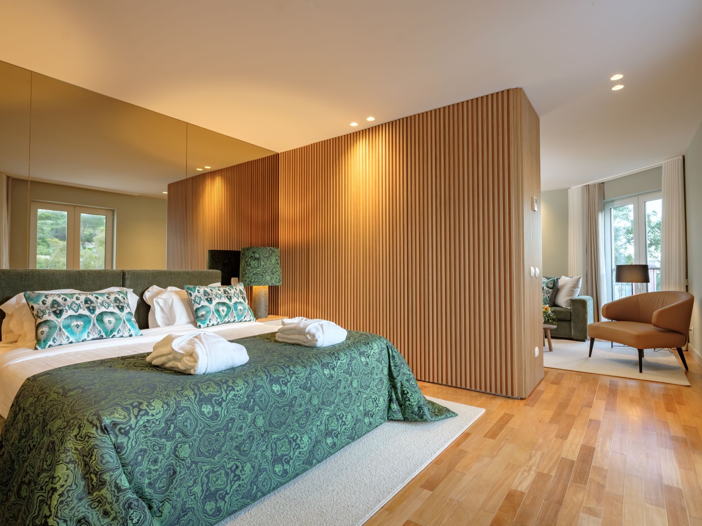 A modern bedroom with a large bed, a wooden accent wall, and a view of the outdoors.
