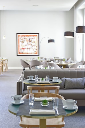 Un comedor moderno con mesas redondas, asientos acolchados y un cuadro abstracto grande en la pared.