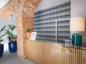 Un área de recepción con un arco de ladrillo, mostrador de madera, pared con diseño y plantas en macetas.