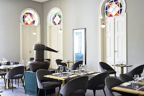 Um restaurante com mesas redondas, cadeiras e uma lareira grande.