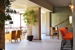 A lobby with a large potted plant, yellow chairs, wooden tables, and orange chairs. - Pure Monchique Hotel by Unlock Hotels (Monchique)