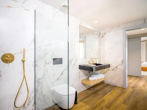 Un baño moderno con ducha envuelta en vidrio, inodoro blanco y tocador con encimera de mármol.