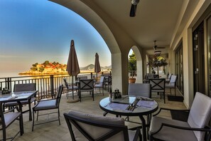 Une terrasse extérieure avec des tables et des chaises, offrant une vue sur une zone côtière avec des bâtiments et des montagnes.