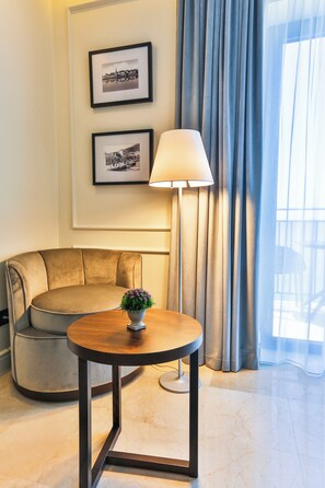 A hotel room with a round wooden table, a beige sofa, a floor lamp, and two framed pictures on the wall. - California (Sveti Stefan)