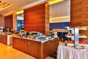 A buffet area with various food stations, a seating area with a tufted chair, and a wooden accent wall. - California (Sveti Stefan)