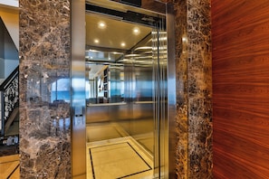 Interior de ascensor con pared de mármol, panel de madera y diseño moderno.