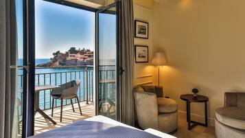 A hotel room with a balcony, a bed, a chair, a table, and a lamp.