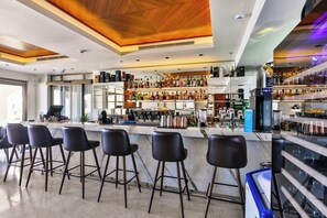 Zona de bar moderna con mostrador de mármol, taburetes negros y una variedad de botellas de licores.