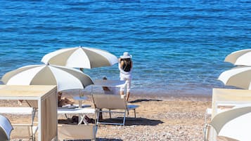 A beach with white umbrellas and chairs, a person in a white outfit, and a clear blue sea.