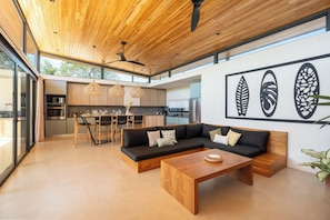 A modern interior with a wooden ceiling, a black sofa, a dining area, and a kitchen visible through large windows. - Spectacular Villa in Avellanas (Santa Cruz)