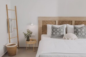 Ein Bett mit gemusterten Kissen, eine Holzleiter, ein kleiner runder Tisch mit einer Pflanze und ein Korbwäsche.