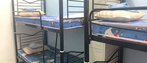 A bunk bed room with a blue mattress featuring cartoon characters, a white pillow, and a small storage cabinet.