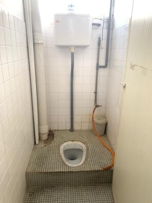 A small, tiled bathroom with a squat toilet, a water tank, and a hose. - Spot ON 89872 Kuantan Backpackers (Kuantan)